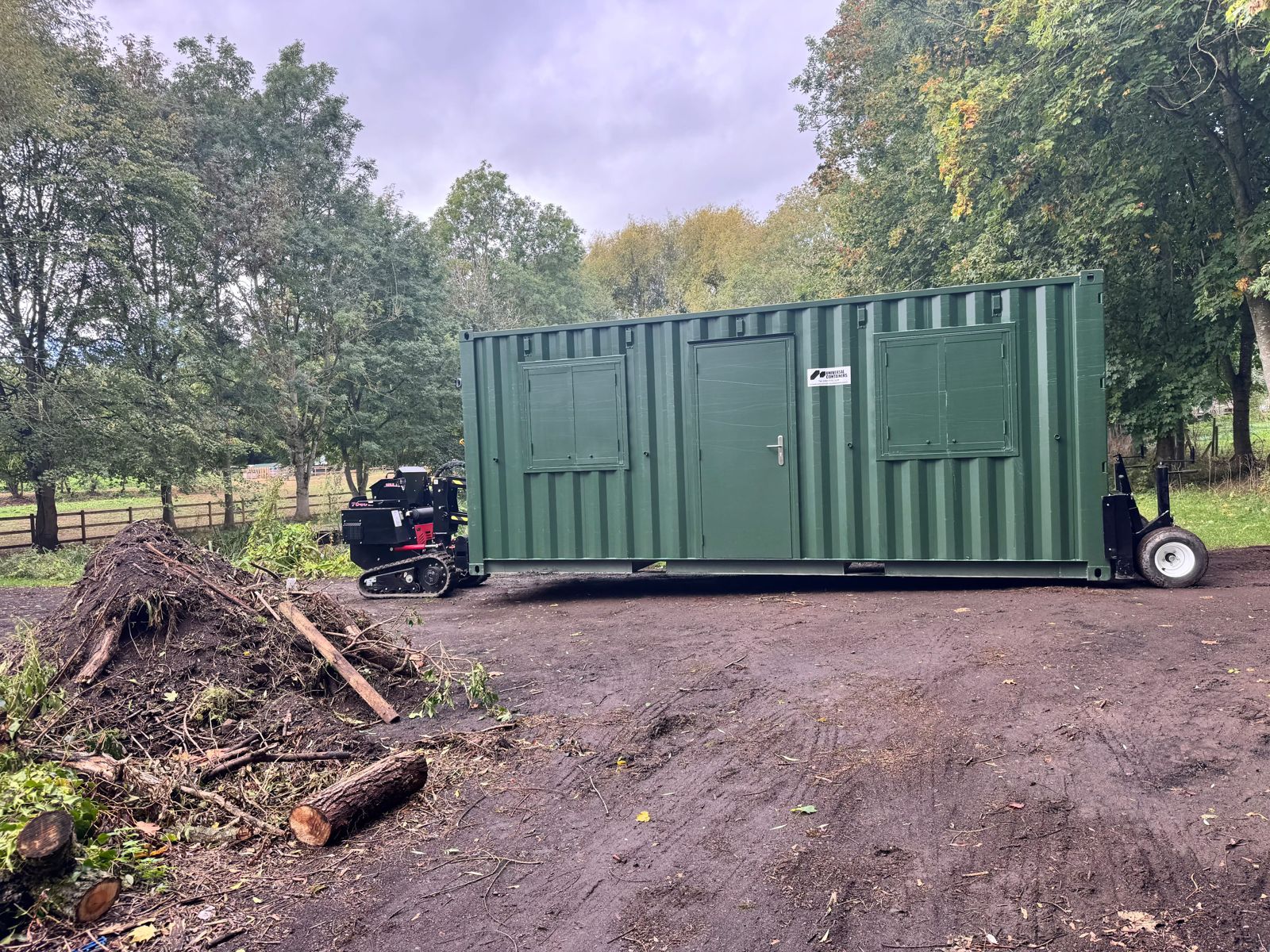 Green shipping container beside an area of dirt and debris