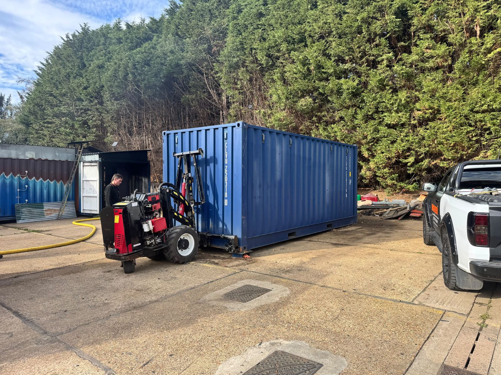 Blue shipping container being handled by container moving machinery on a concrete surface
